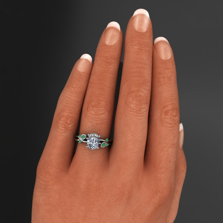 1.5 carat oval engagement ring with leaves and green sapphires on a hand
