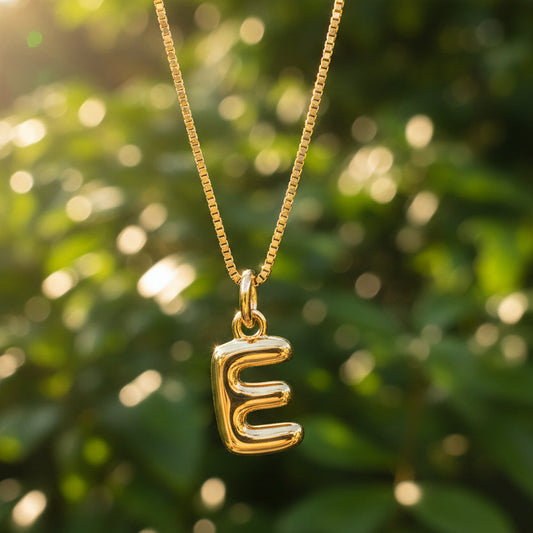 Gold necklace with a letter 'E' pendant on a green leafy background